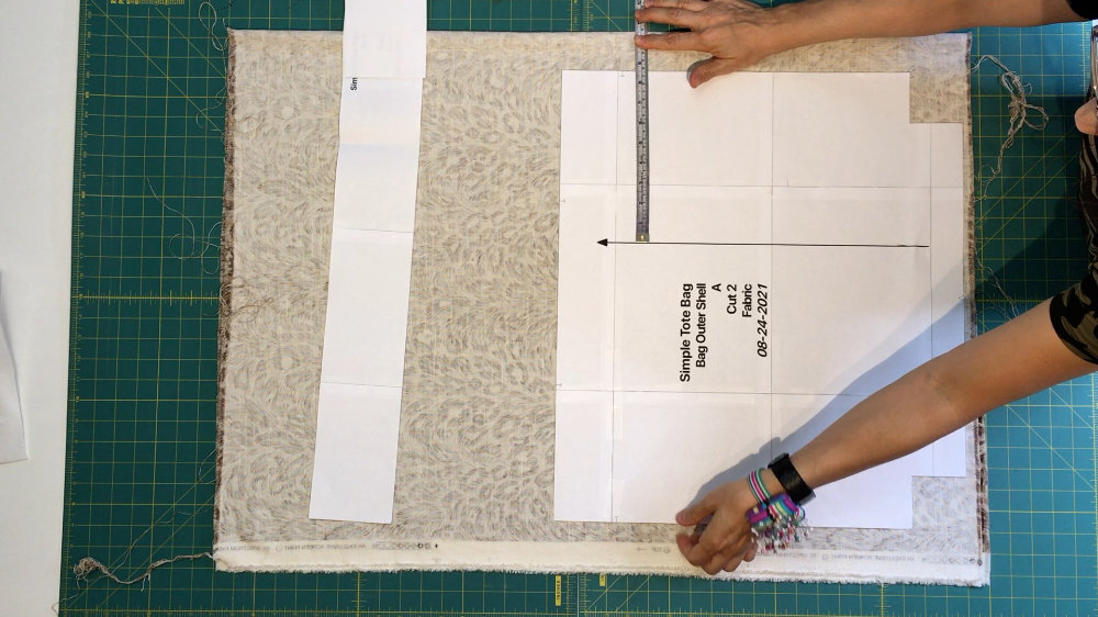 Photo of laying a pattern on fabric using a tape measure to make sure it is lined up properly